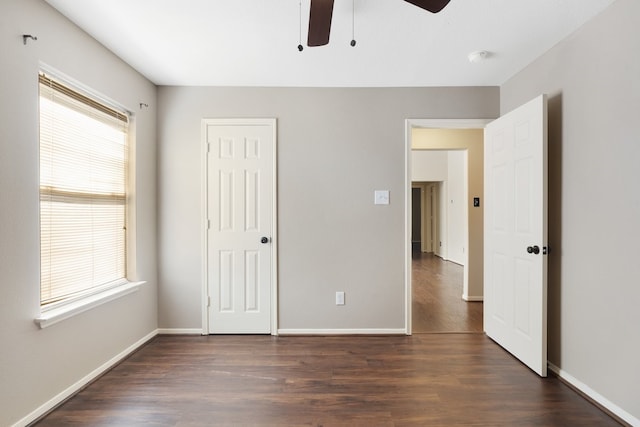 unfurnished bedroom with a closet, dark wood finished floors, a ceiling fan, and baseboards