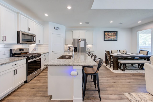 kitchen featuring visible vents, light wood-style flooring, appliances with stainless steel finishes, a sink, and a kitchen bar