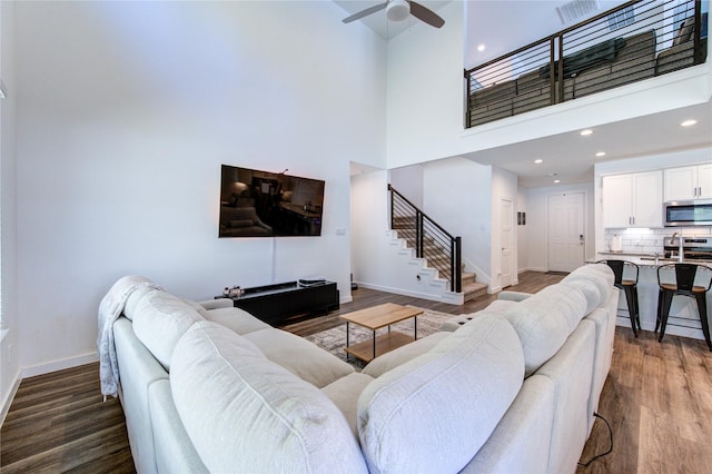 living room with a high ceiling, a ceiling fan, baseboards, stairs, and dark wood-style floors