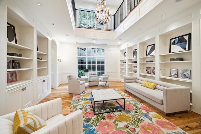 living room with a chandelier, a decorative wall, built in shelves, and wood finished floors