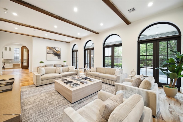 living room with arched walkways, recessed lighting, visible vents, light wood-style floors, and beamed ceiling