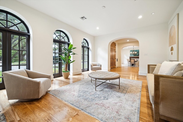 living area with baseboards, visible vents, arched walkways, light wood-style floors, and recessed lighting