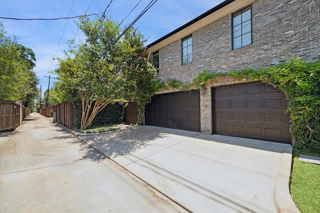 view of property exterior with a garage, concrete driveway, brick siding, and fence