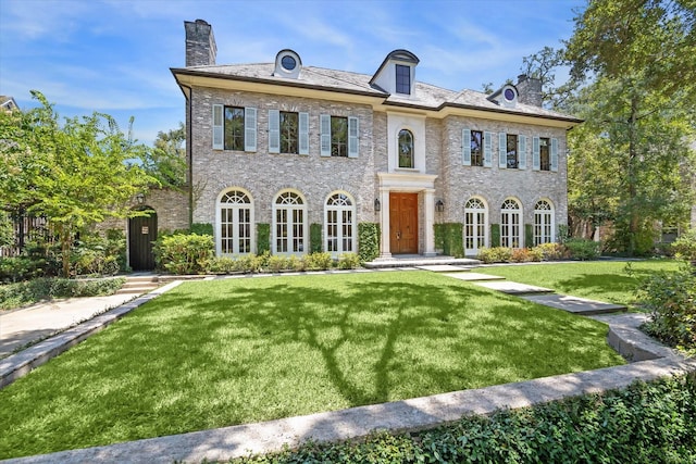 colonial-style house featuring a high end roof, a chimney, and a front lawn