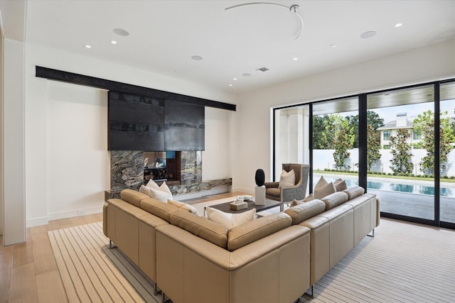 living area featuring baseboards, recessed lighting, a fireplace, and light wood-style floors