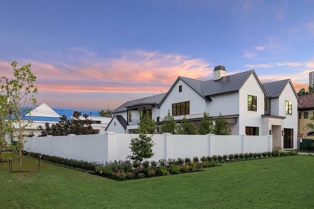 view of home's exterior with stucco siding, a lawn, a standing seam roof, metal roof, and fence