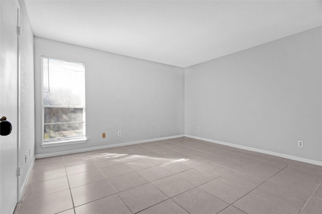 spare room with tile patterned floors, a wealth of natural light, and baseboards