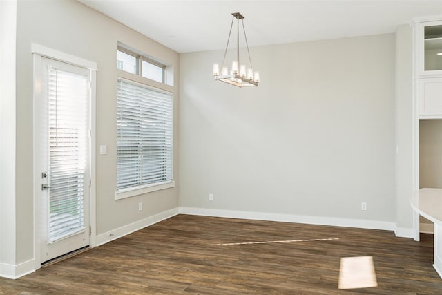 unfurnished dining area with an inviting chandelier, baseboards, and dark wood-type flooring