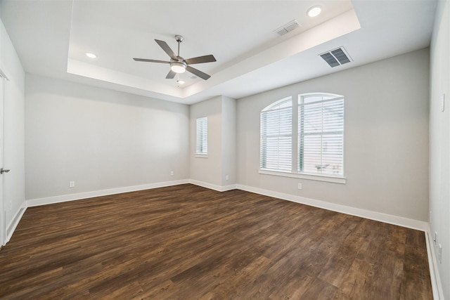 spare room featuring baseboards, visible vents, a raised ceiling, and dark wood-style flooring