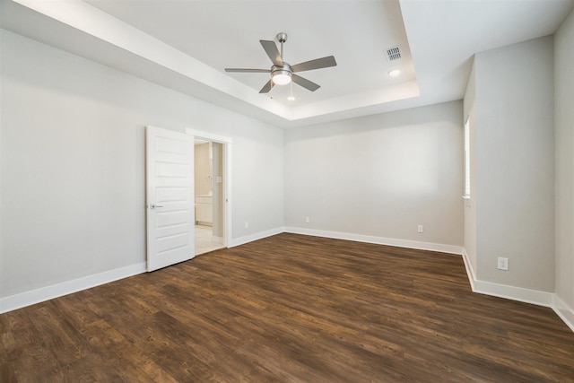 spare room featuring ceiling fan, visible vents, baseboards, a tray ceiling, and dark wood finished floors