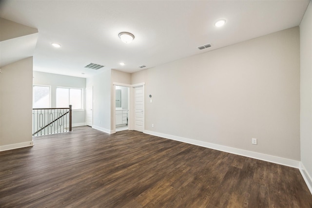 empty room with dark wood-type flooring, visible vents, and baseboards