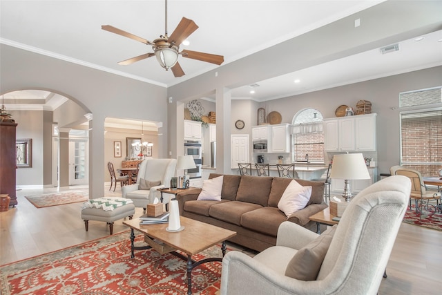 living area featuring visible vents, arched walkways, ceiling fan, light wood-style flooring, and crown molding