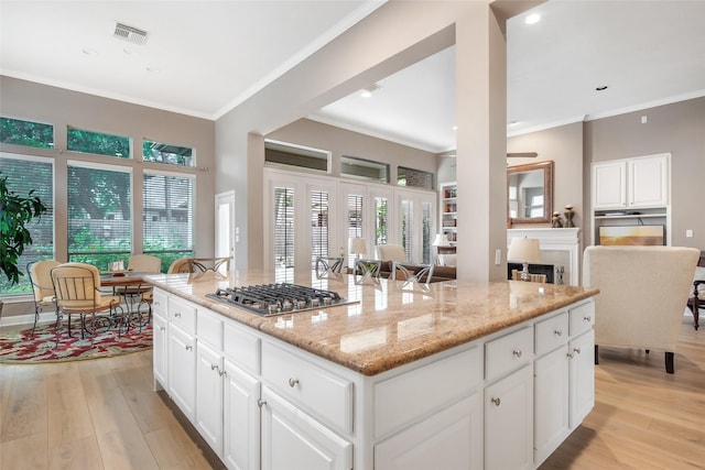 kitchen featuring stainless steel gas cooktop, ornamental molding, white cabinets, light stone countertops, and light wood-type flooring