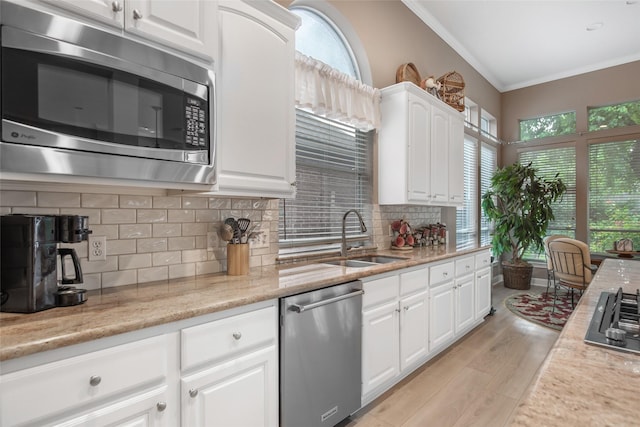 kitchen with stainless steel appliances, a sink, backsplash, light wood finished floors, and crown molding