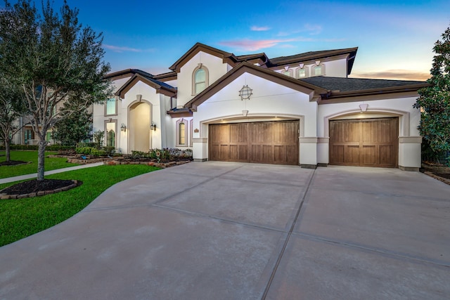 mediterranean / spanish-style house with driveway, a lawn, an attached garage, and stucco siding