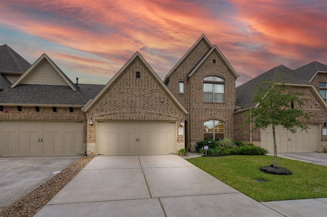 french provincial home featuring concrete driveway, brick siding, a yard, and an attached garage