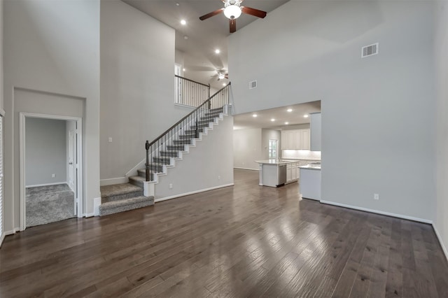 unfurnished living room featuring dark wood-style floors, stairway, visible vents, and a ceiling fan