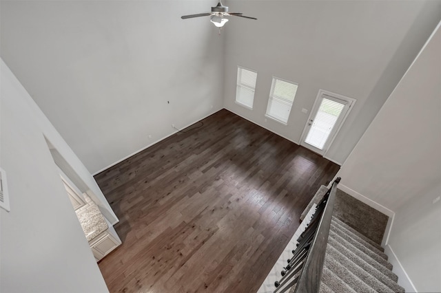 unfurnished living room with a high ceiling, dark wood-style flooring, a ceiling fan, baseboards, and stairs