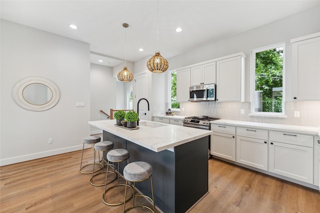 kitchen with light stone counters, light wood finished floors, stainless steel appliances, backsplash, and a sink