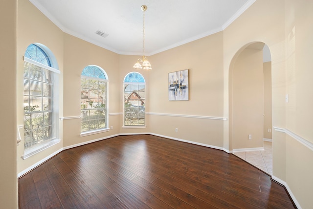 empty room with a chandelier, wood finished floors, visible vents, and baseboards