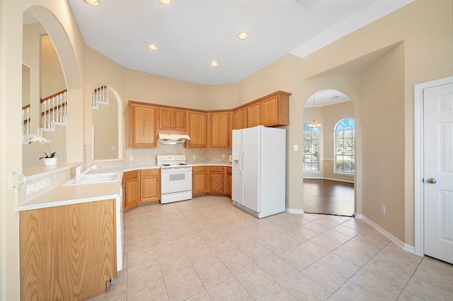 kitchen with white appliances, arched walkways, a sink, light countertops, and under cabinet range hood