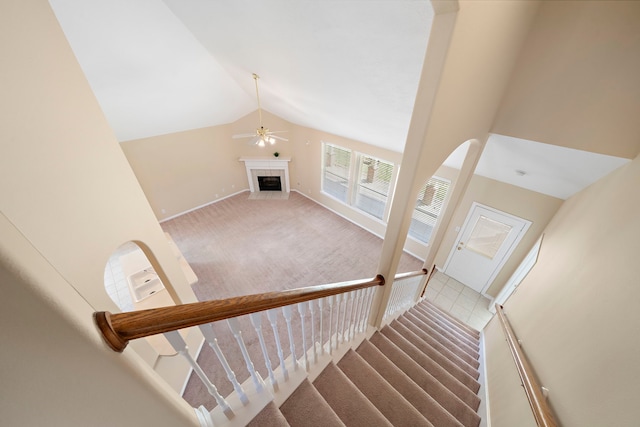 staircase featuring a ceiling fan, a tile fireplace, carpet, baseboards, and vaulted ceiling