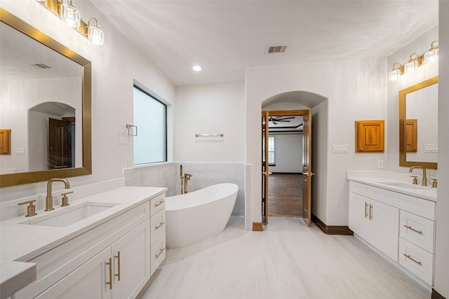 bathroom with two vanities, a freestanding tub, visible vents, and a sink