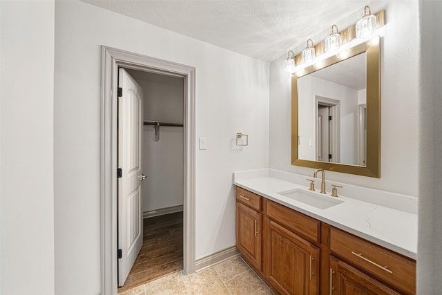 bathroom featuring baseboards, vanity, a textured ceiling, and a spacious closet