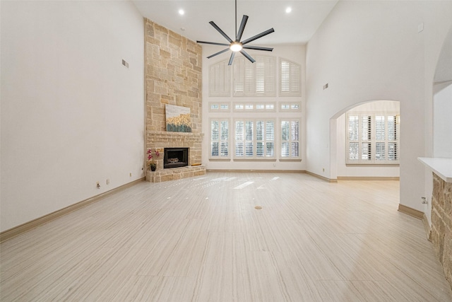 unfurnished living room with a fireplace, visible vents, a high ceiling, ceiling fan, and baseboards