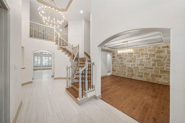 foyer with arched walkways, a tray ceiling, wood finished floors, a chandelier, and stairs