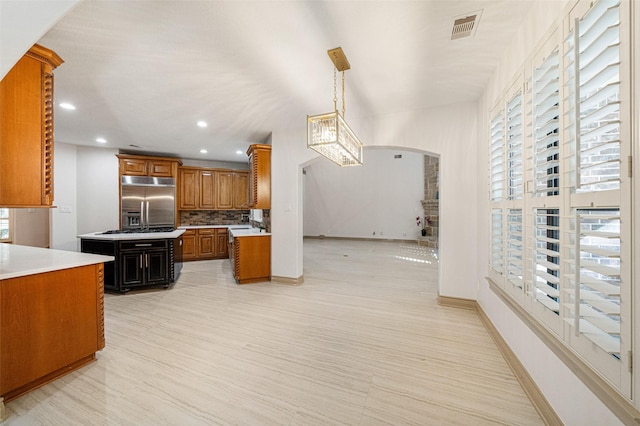 kitchen featuring arched walkways, built in fridge, visible vents, light countertops, and brown cabinets