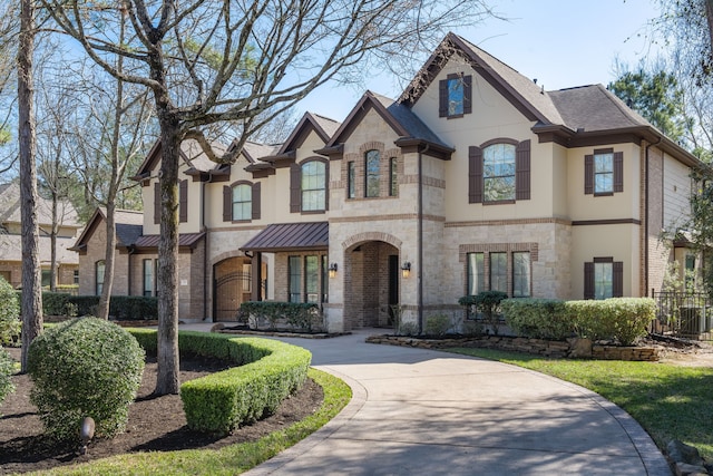 french country home featuring concrete driveway, brick siding, stone siding, and stucco siding