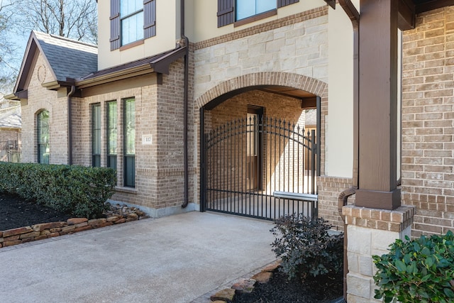 doorway to property featuring a shingled roof, a gate, and brick siding