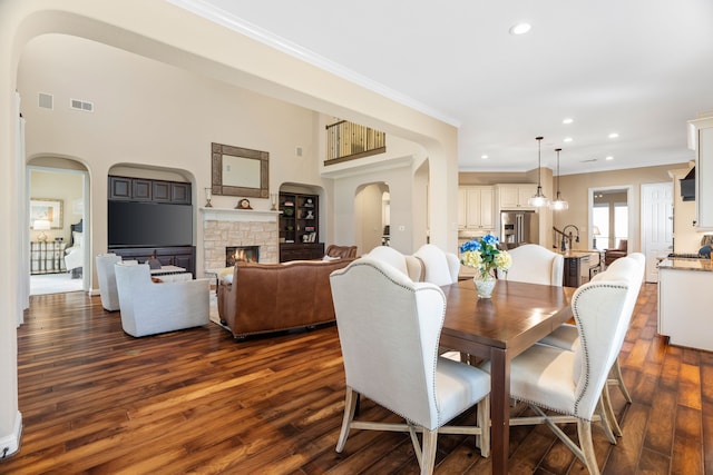 dining room featuring arched walkways, dark wood-type flooring, a fireplace, and visible vents