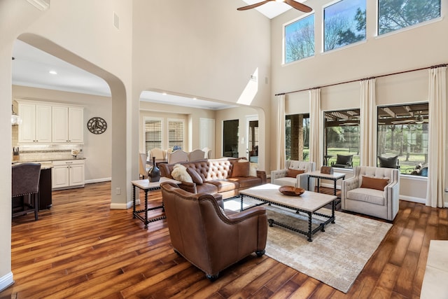 living area with a ceiling fan, arched walkways, dark wood-style flooring, and baseboards