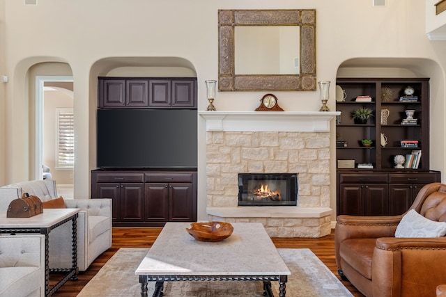 living room featuring a stone fireplace and dark wood-type flooring