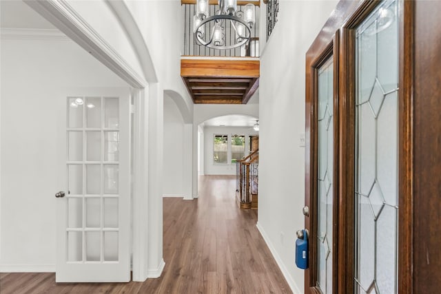 hall featuring stairs, arched walkways, baseboards, and wood finished floors