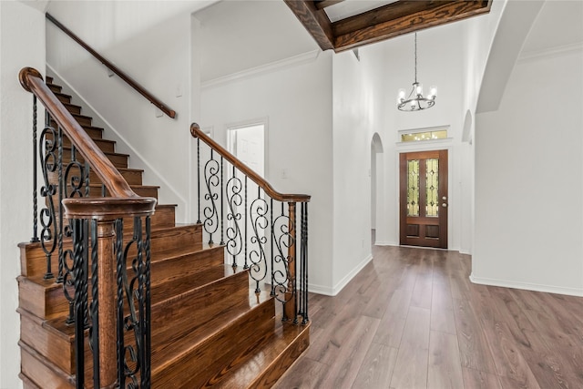 foyer with arched walkways, a notable chandelier, wood finished floors, baseboards, and beamed ceiling