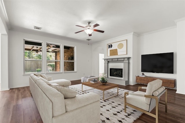 living area with a fireplace, visible vents, ornamental molding, ceiling fan, and wood finished floors