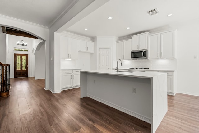 kitchen with arched walkways, stainless steel microwave, visible vents, a sink, and wood finished floors