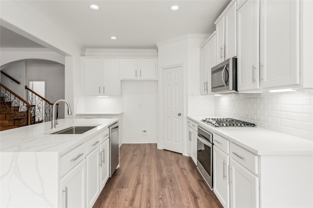 kitchen with stainless steel appliances, light wood-style floors, ornamental molding, white cabinetry, and a sink