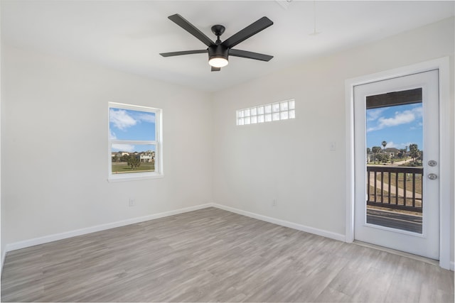 spare room featuring attic access, light wood-style flooring, baseboards, and a ceiling fan