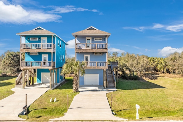 beach home featuring a garage, concrete driveway, a balcony, stairway, and a front lawn