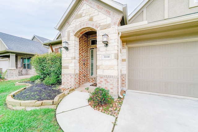 view of exterior entry with a garage, stone siding, and brick siding