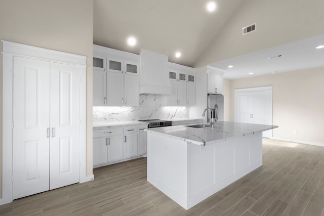 kitchen featuring white cabinets, stainless steel fridge with ice dispenser, custom range hood, a kitchen island with sink, and a sink