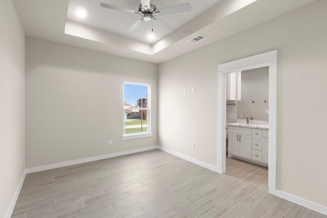 unfurnished bedroom featuring visible vents, baseboards, light wood-style floors, a raised ceiling, and ensuite bath