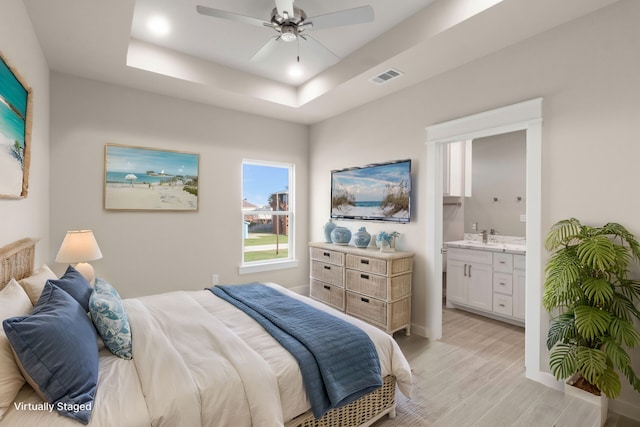 bedroom with connected bathroom, visible vents, baseboards, light wood-type flooring, and a raised ceiling