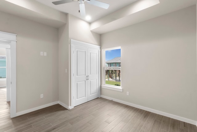 unfurnished bedroom featuring light wood finished floors, a ceiling fan, baseboards, and a closet