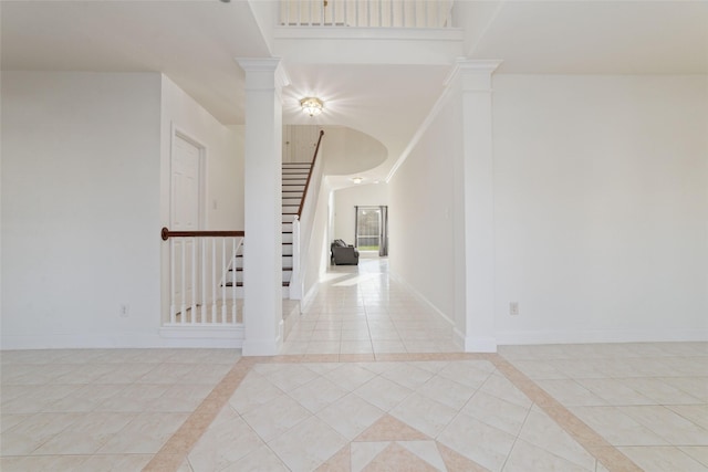 empty room with a high ceiling, light tile patterned flooring, decorative columns, and baseboards