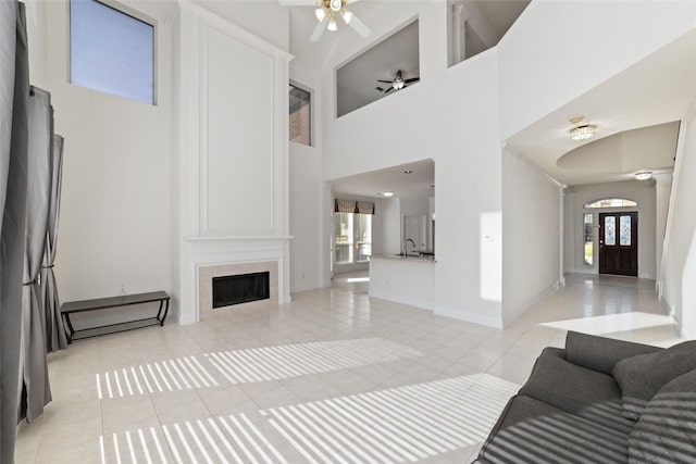living room featuring a large fireplace, light tile patterned floors, a ceiling fan, baseboards, and a towering ceiling